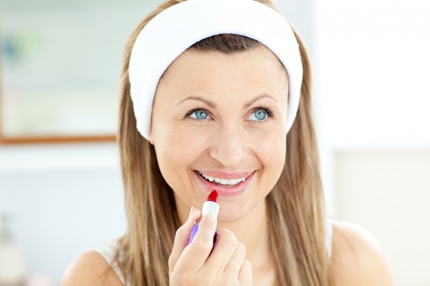 Foto giovane donna graziosa che utilizza un rossetto rosso nel bagno