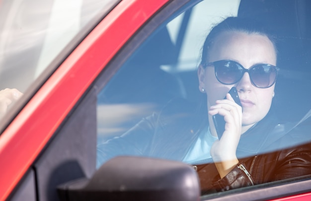 スマートフォンを使用してかなり若い女性、車を運転しながら携帯電話、交通機関の概念