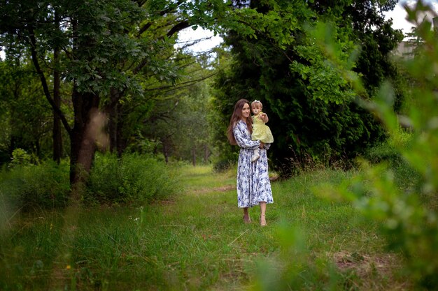 Pretty young woman walks carrying little baby girl at the garden