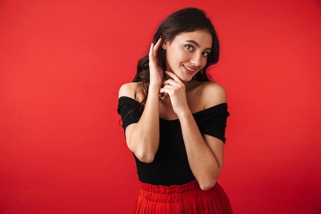 Pretty young woman wearing a dress standing isolated over red, posing