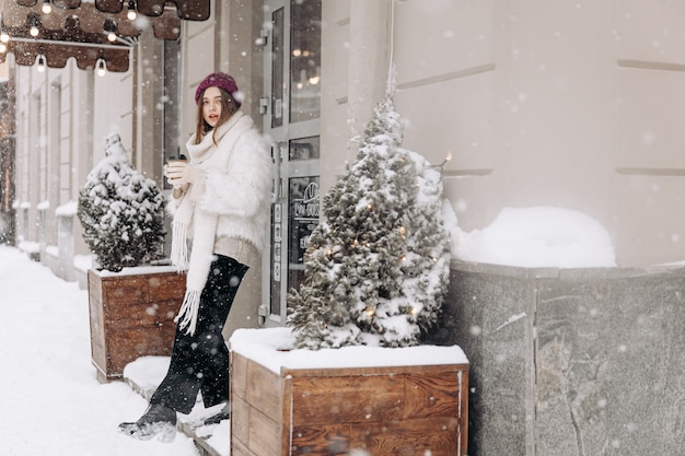 Pretty young woman in winter outfit walking during snowfall