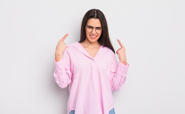 Pretty young woman with a bad attitude looking proud and aggressive, pointing upwards or making fun sign with hands