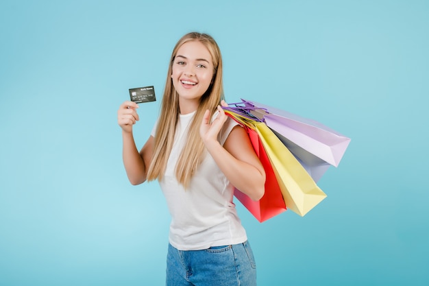 クレジットカードと青で分離されたカラフルなショッピングバッグを持つかなり若い女性