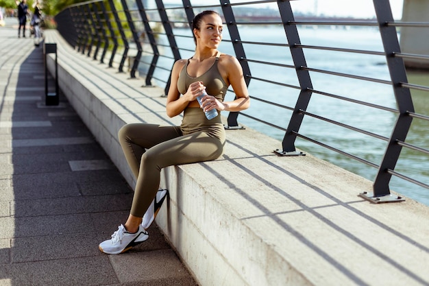 Pretty young woman with earphones takes a break after running\
in urban area