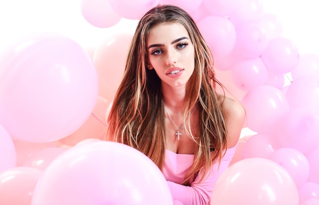 Pretty young woman with long hair lying in pink balloons. Party mood and Celebration concept.