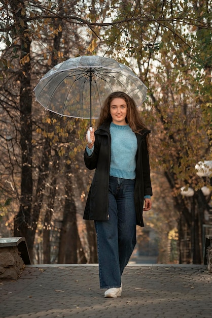 Piuttosto giovane donna con capelli lussureggianti in piedi con ombrello trasparente in autunno parco foto di donna nel parco