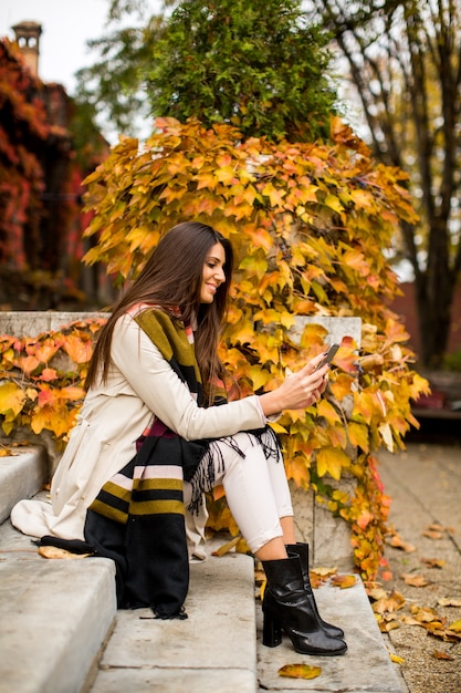 Pretty young woman with mobile phone in autumn park