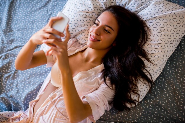 Pretty young woman with mobile phone on bed