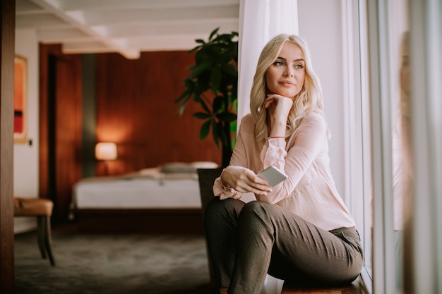 Pretty young woman with mobile phone by the window