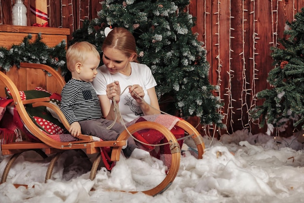 Pretty young woman with oneyearold child playing by Christmas tree