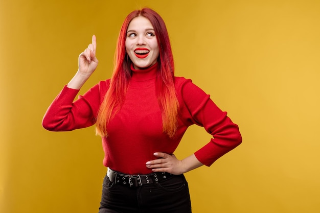 Pretty young woman with red hair pointing finger on yellow background