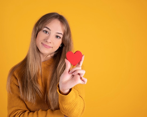 Foto giovane donna graziosa con un cuore rosso in sue mani, spazio giallo