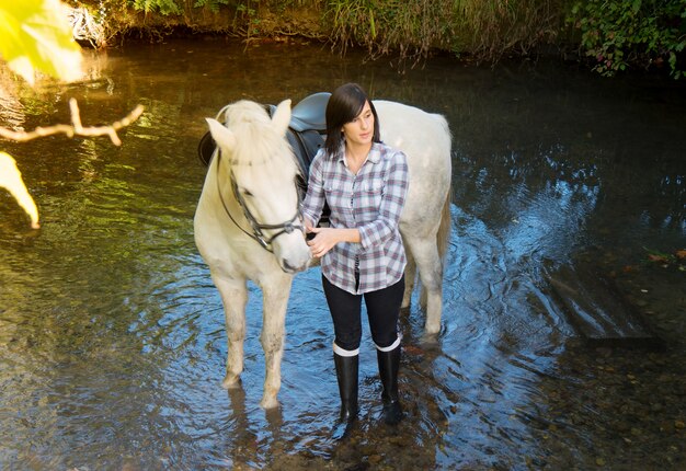 Pretty young woman with white horse riding in the river