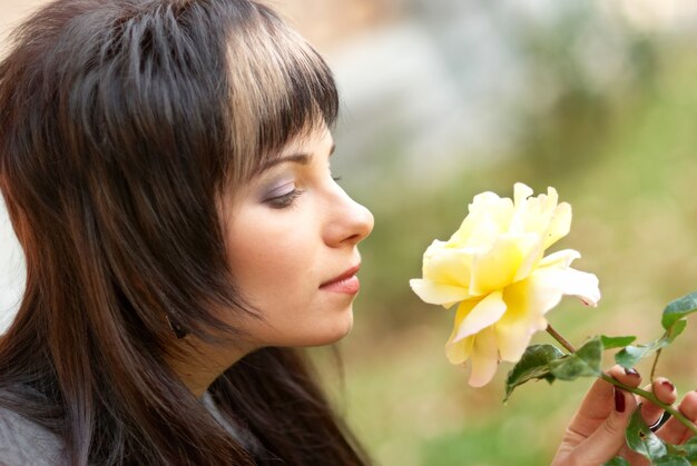 庭で黄色いバラを持つかなり若い女性