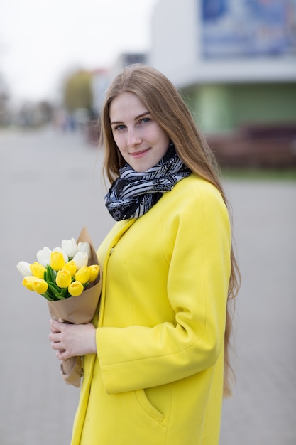 Довольно молодая женщина в желтом пальто с белыми и желтыми цветами