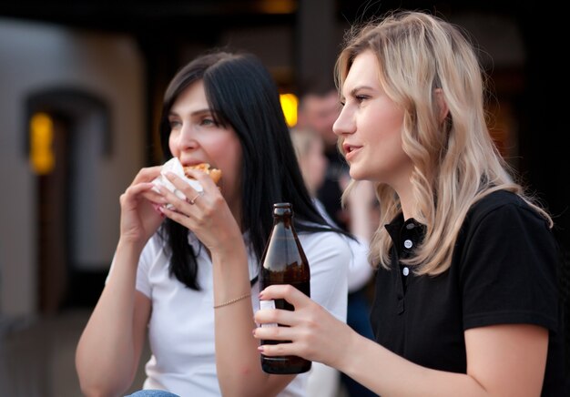 路上でハンバーガーとビールを屋外で食べるかなり若い女性