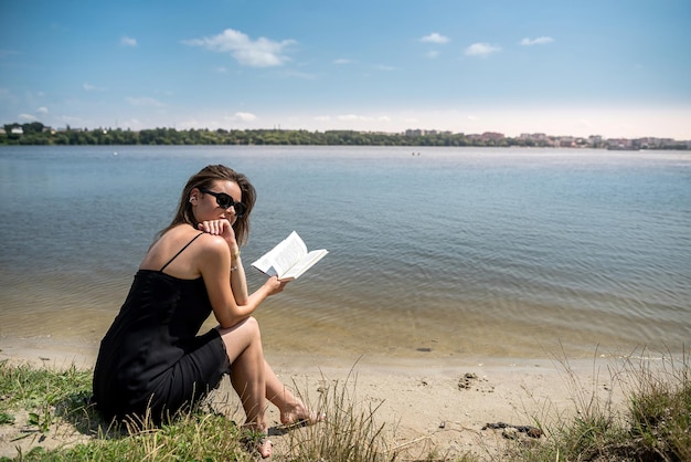 Prety jonge vrouw in zomerdag lees boek in de buurt van een meerlevensstijl