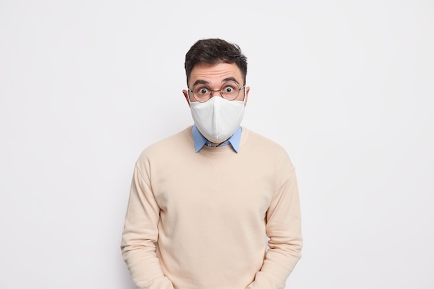 Prevent virus spread. shocked man wears face mask recommends\
wearing protective measures during coronavirus pandemic dressed in\
sweater