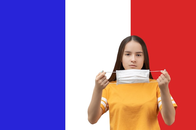 写真 フランスでのコロナウイルスの予防若い女の子は、コピースペースで旗の背景に抗菌医療マスクを着用します