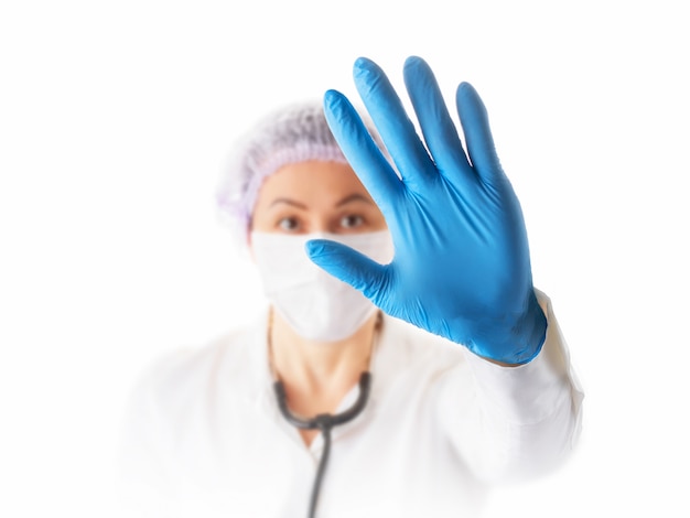 예방 및 감염 개념을 중지합니다. 코로나 바이러스를 중지하십시오. 중지 제스처를 보여주는 의료 보호 마스크에 여성 의사 또는 간호사. 손에 중점을 둡니다.
