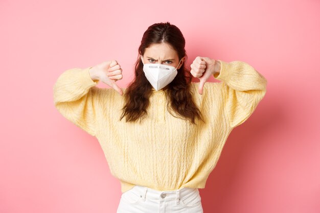 Preventive measures health care concept angry and disappointed woman condemn something bad showing thumbs down and frowning dislike wearing medical respirator during covid