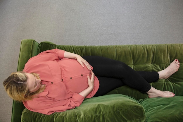 A prgnant woman relaxing on a green sofa holding her baby bump