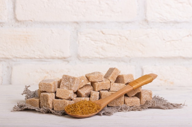 Photo pricked cane sugar in cubes on a linen cloth and a wooden spoon