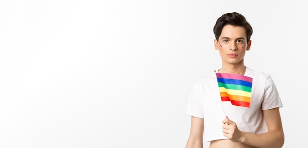 Pride and lgbtq concept waist up shot of attractive anrogynous man holding rainbow flag having glitt