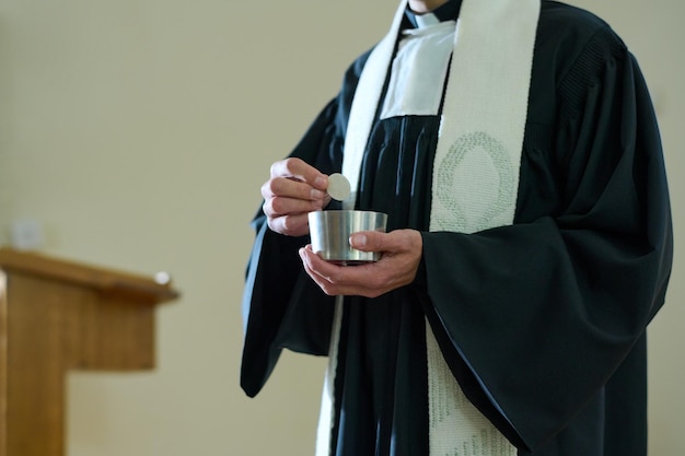 Foto sacerdote della chiesa cattolica in tonaca con in mano una tazzina con pane azzimo