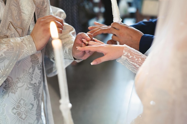Il sacerdote consacra le fedi nuziali alle dita degli sposi. tradizione e rituale del matrimonio. mani di una giovane coppia in chiesa.