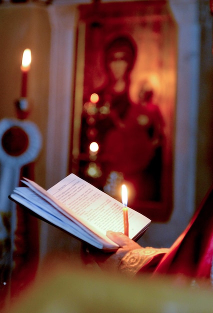 priest holding a candle in the night and reading a bible