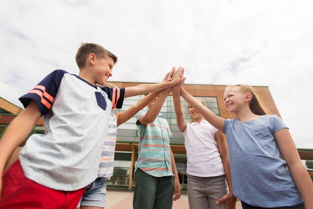 primary education, friendship, childhood and people concept - group of children or students making high five at school yard