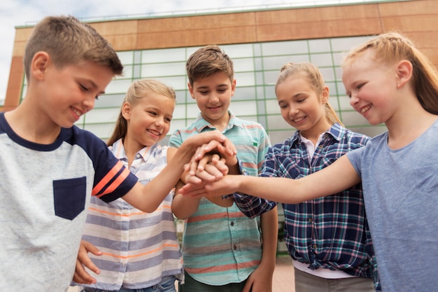 Foto istruzione primaria, amicizia, infanzia e concetto di persone - gruppo di studenti delle scuole elementari felici con le mani in alto all'aperto