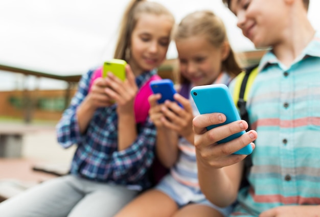 초등 교육, 우정, 유년기, 기술 및 사람 개념 - 야외에서 스마트폰과 배낭을 들고 다니는 행복한 초등학생 그룹