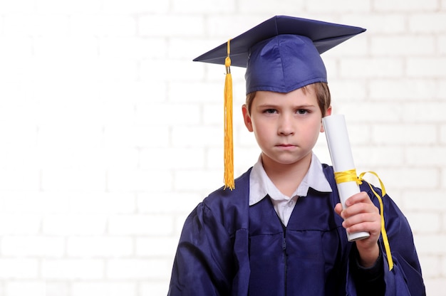 Photo primary school boy in cup and gown posing with diploma.