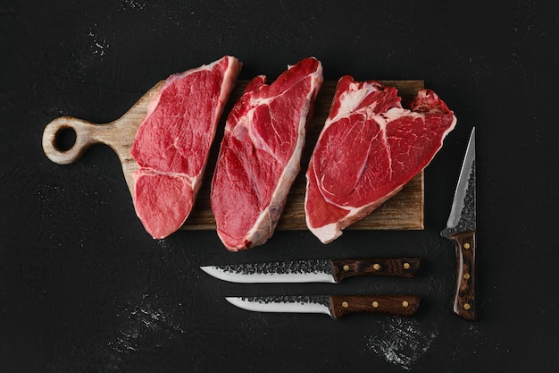Prime black angus beef steaks on wooden board: top sirloin, strip steeak and top round roast