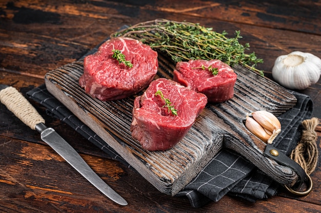 Prime rauwe filet mignon steaks op een houten bord met tijm en knoflook. Donkere houten achtergrond. Bovenaanzicht.