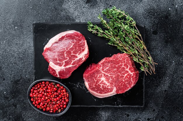 Prime Raw Fillet Mignon tenderloin steaks with thyme. Black background. Top view.