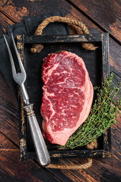 요리할 준비가 된 허브를 곁들인 원시 뉴욕 쇠고기 고기 스테이크 나무 배경 평면도