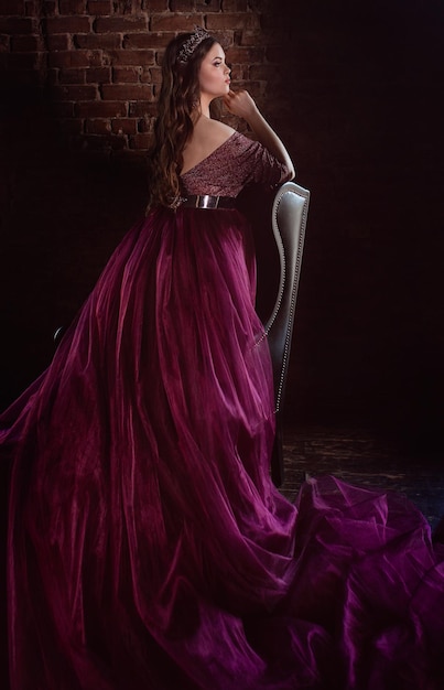 princess (queen) in long purple queen's dress and crown near leather armchair