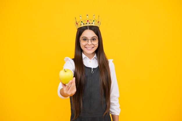 Prinses kind in koningin kroon houd appel geïsoleerd op gele achtergrond Tienermeisje slijtage diadeem Gelukkig meisje gezicht positieve en lachende emoties