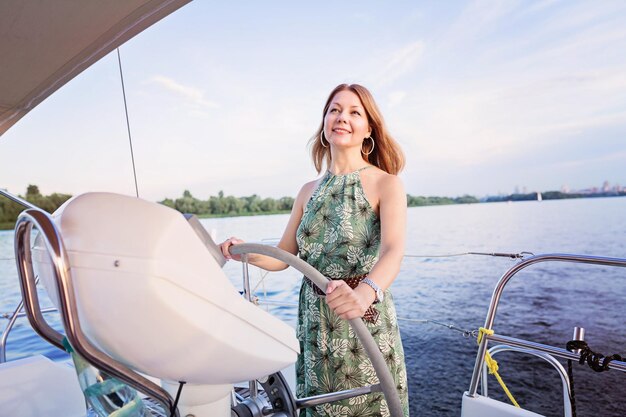 Pritty lady skipper in a long dress holding the helm of the ship