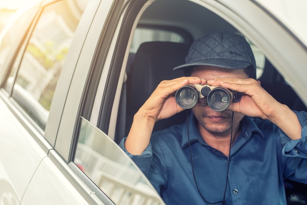 Agente investigativo privato che si siede dentro l'automobile che fotografa con la macchina fotografica di slr