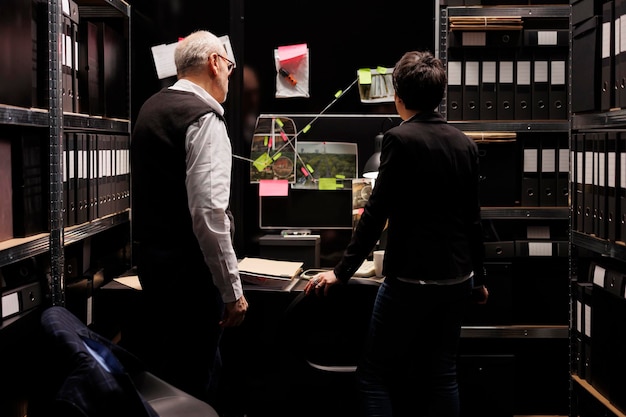 Private detectives analyzing evidence board, working overtime at criminal case in arhive room. Criminology department workers discussing missing person report, planning solution to catch suspect