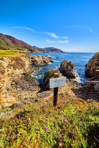 Private no entry sign on fence next to stunning west coast\
ocean with rocky cliffs