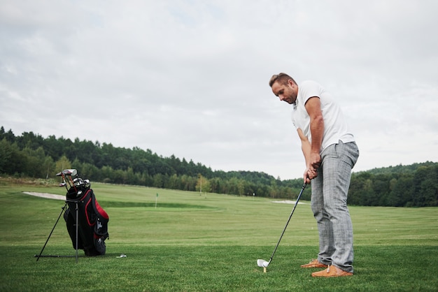 Pro golf player aiming shot with club on course. Male golfer on putting green about to take the hit