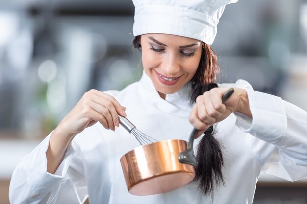 Foto la donna professionista lavora come chef in cucina, sbattendo e tenendo in mano una padella di rame.