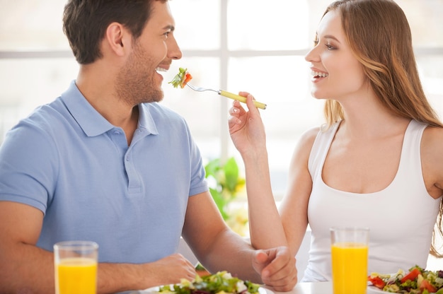 Probeer mijn maaltijd! Mooi jong stel zit samen aan tafel terwijl een vrouw haar vriendje salade voedt