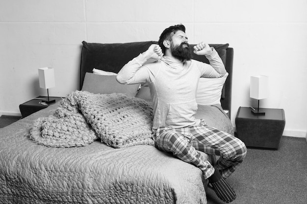 Probleem met vroeg opstaan Vroeg opstaan Tips om vroeg op te staan Man bebaarde hipster slaperig gezicht pyjama wakker worden slaapkamer interieur Dagelijks schema voor een gezonde levensstijl Rust en ontspanning