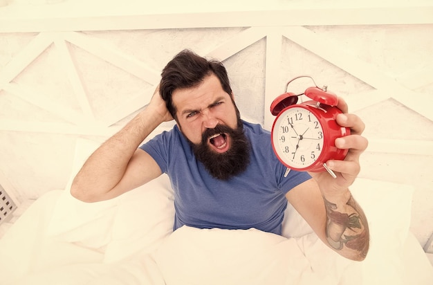 Problem early morning awakening Why you suffering in mornings Get up with alarm clock Waking up early Man bearded sleepy face bed with alarm clock in bed Terrible noise Turn off ringing